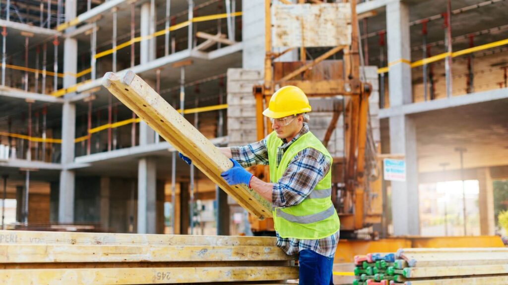Trabalhador em canteiro de obras manuseando material de construção com EPIs completos. Ilustra a importância da conformidade técnica e das normas ABNT e Sabesp para a segurança da obra.